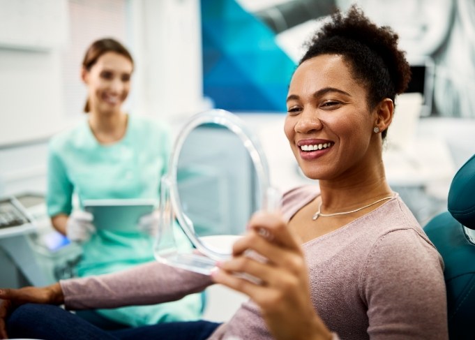 Woman checking her smile in mirror at dental office