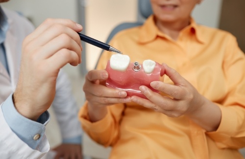 Showing a patient a model of dental implant between two teeth