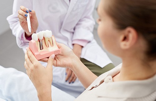 Dentist in white coat pointing to model dental implant held by patient with white pen