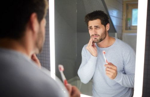 Man with toothbrush rubbing his jaw in pain