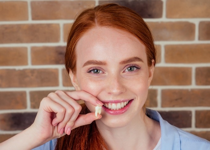 Red haired woman holding a tooth and smiling